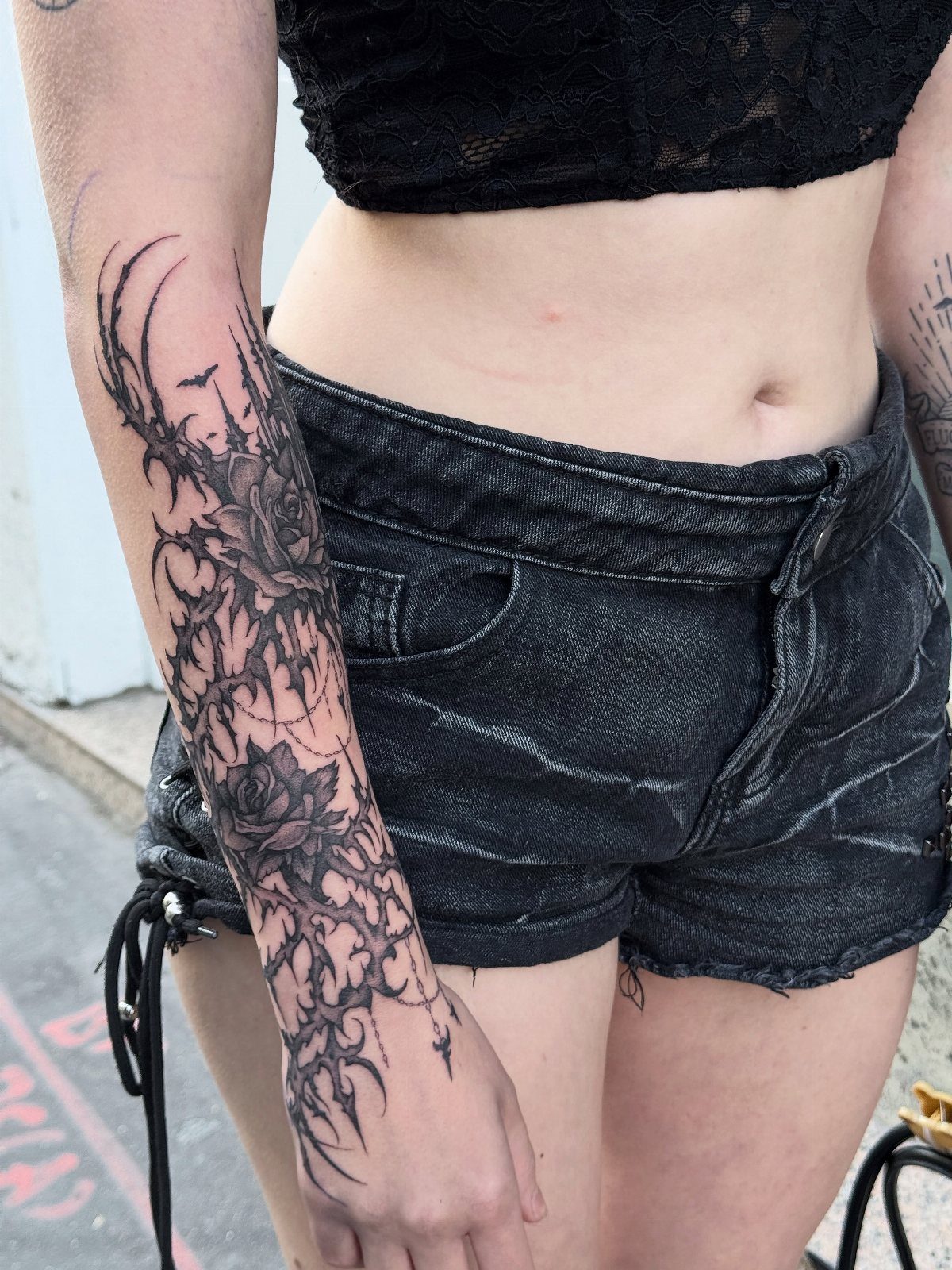 Forearm tattoo of black roses and thorny vines on a person's arm.