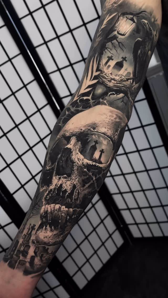 Detailed black and grey tattoo of a skull and graveyard on an arm.