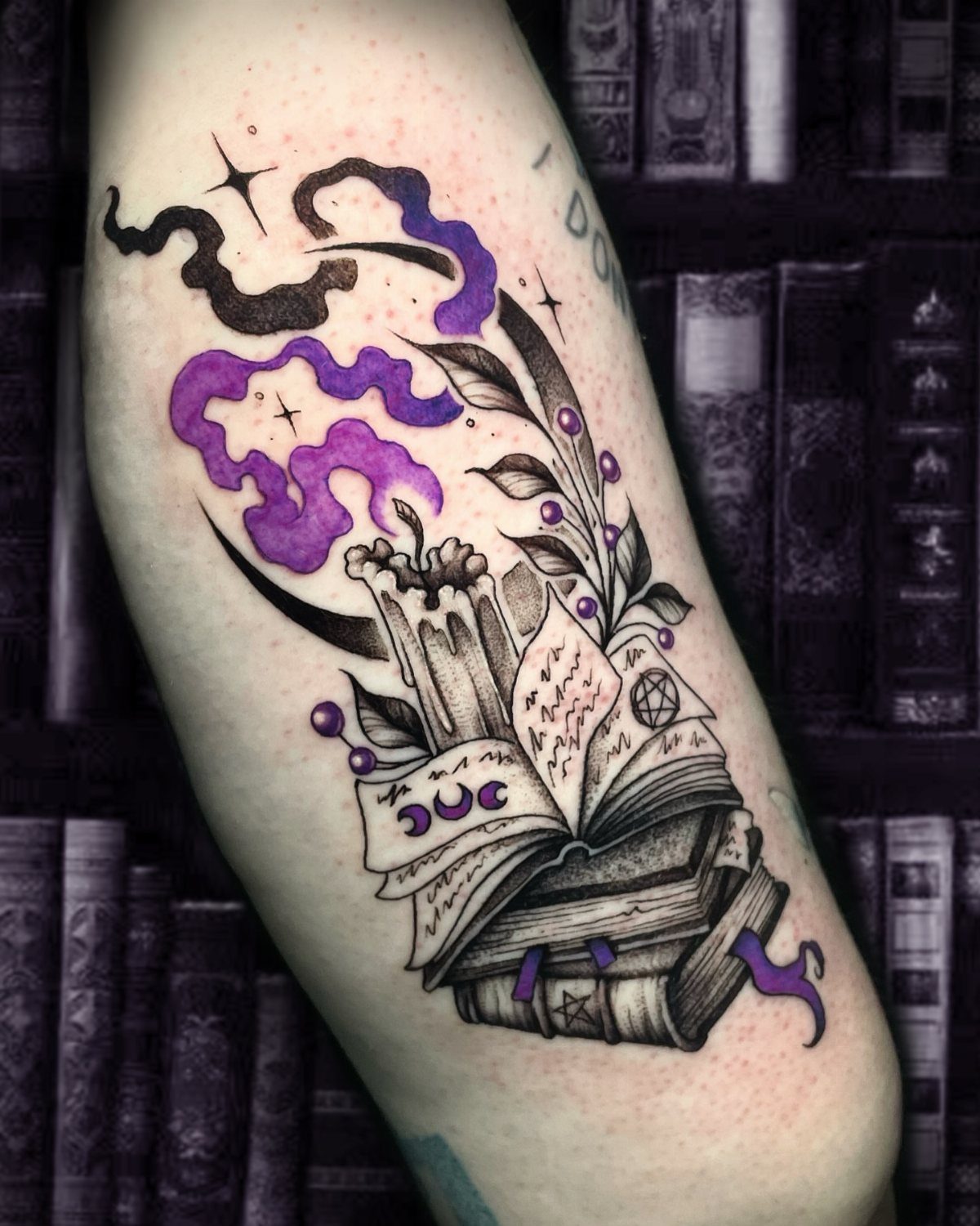 Tattoo of an open spell book with a candle and purple smoke.