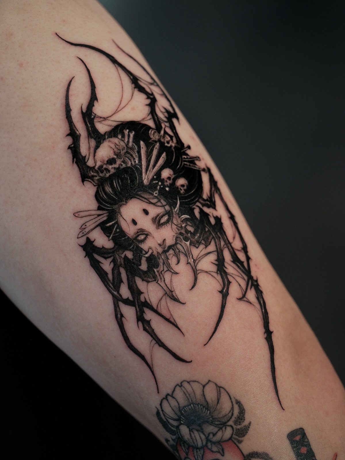 Gothic tattoo of a woman's face merged with a large black spider and skulls.