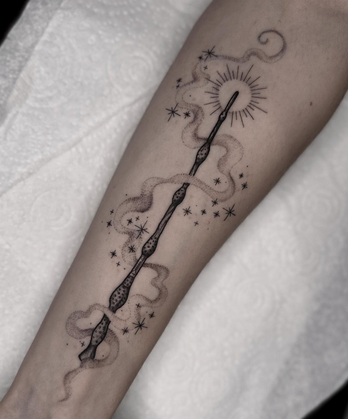 Magic wand tattoo on a forearm with stars and a radiating sunburst tip.