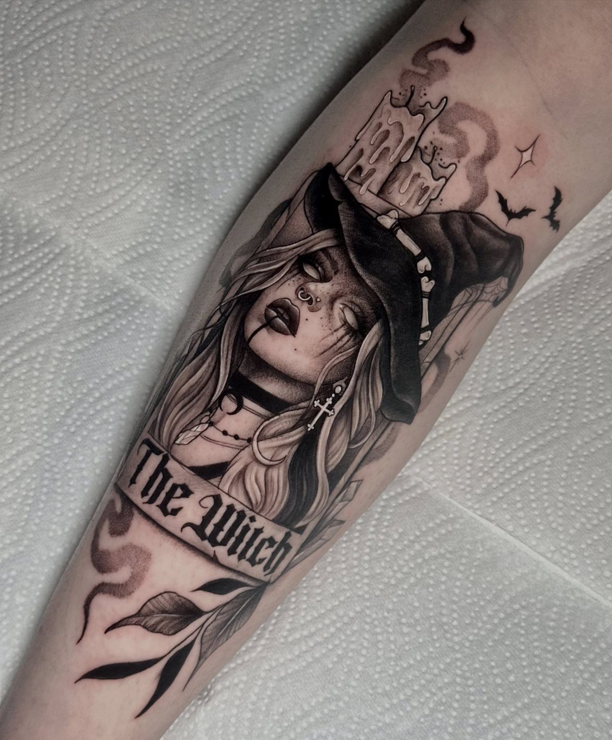 Tattoo of a woman wearing a pointed witch hat with a candle and bats.