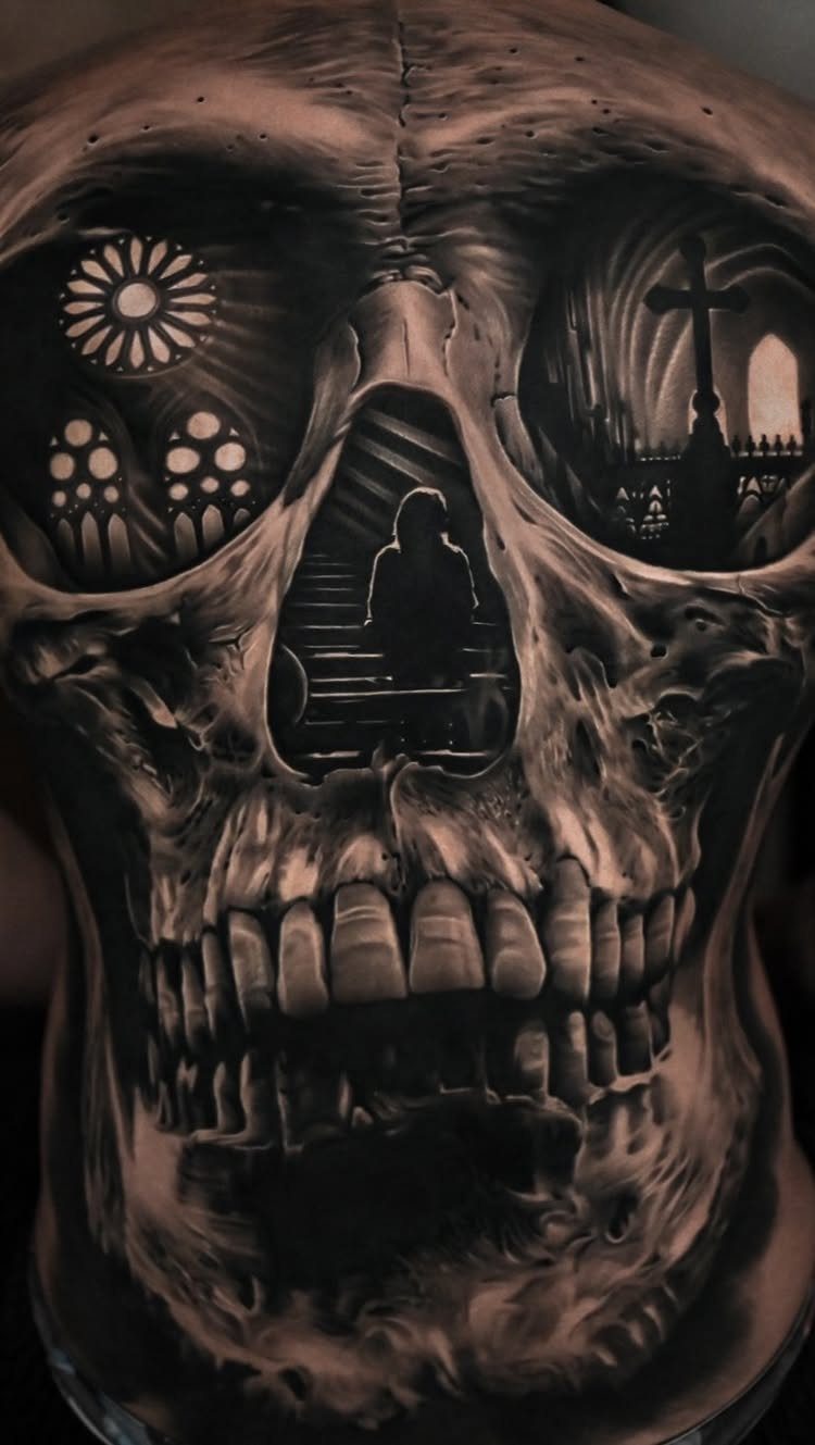 Skull tattoo featuring gothic cemetery and cathedral scenes within the eye sockets.
