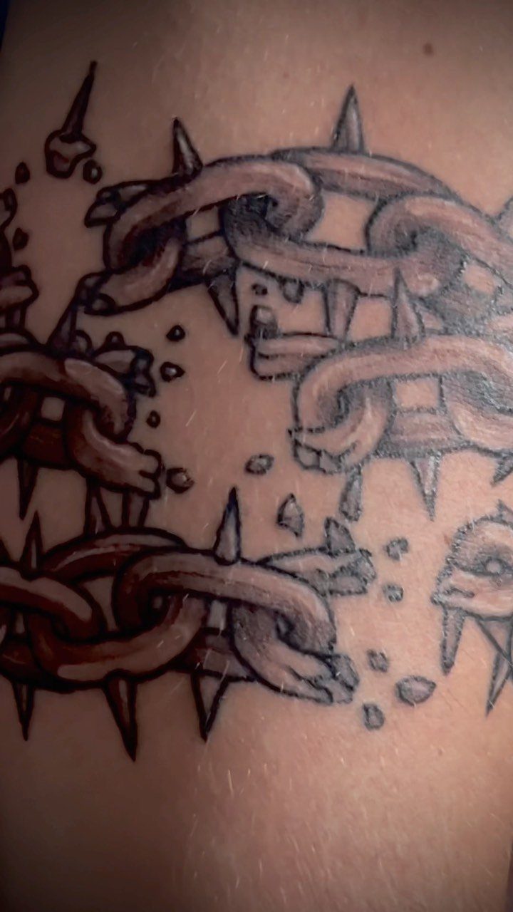 Broken metallic chains tattoo with sharp spikes on human skin.