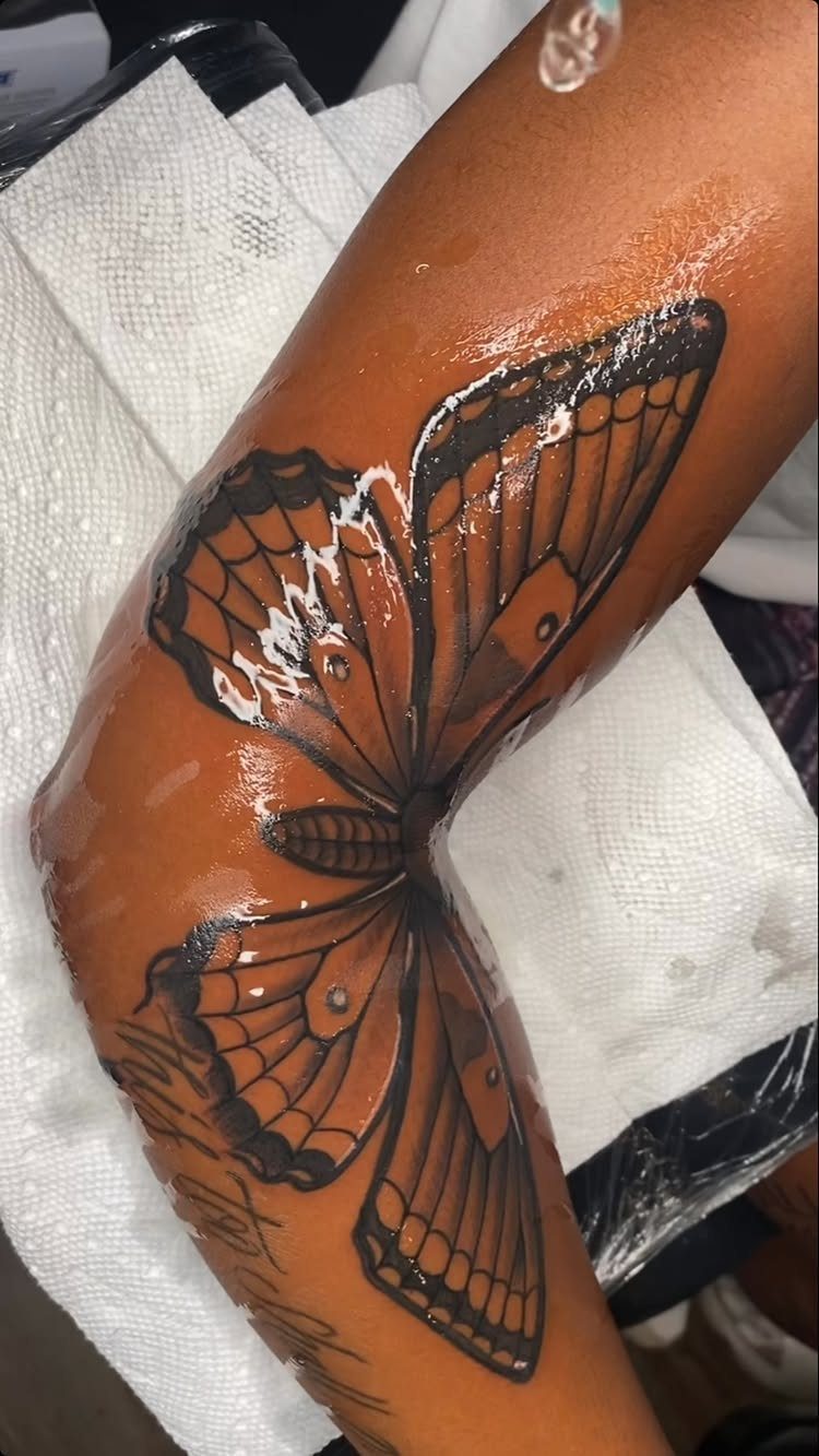 Butterfly tattoo with black outlines on a person's forearm resting on white paper.