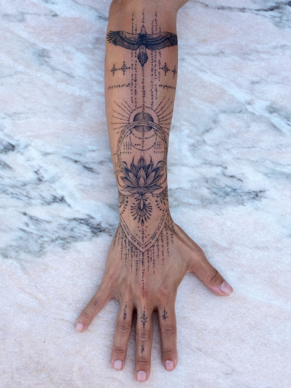 Intricate black ink tattoo on a forearm featuring a central lotus flower and bird.