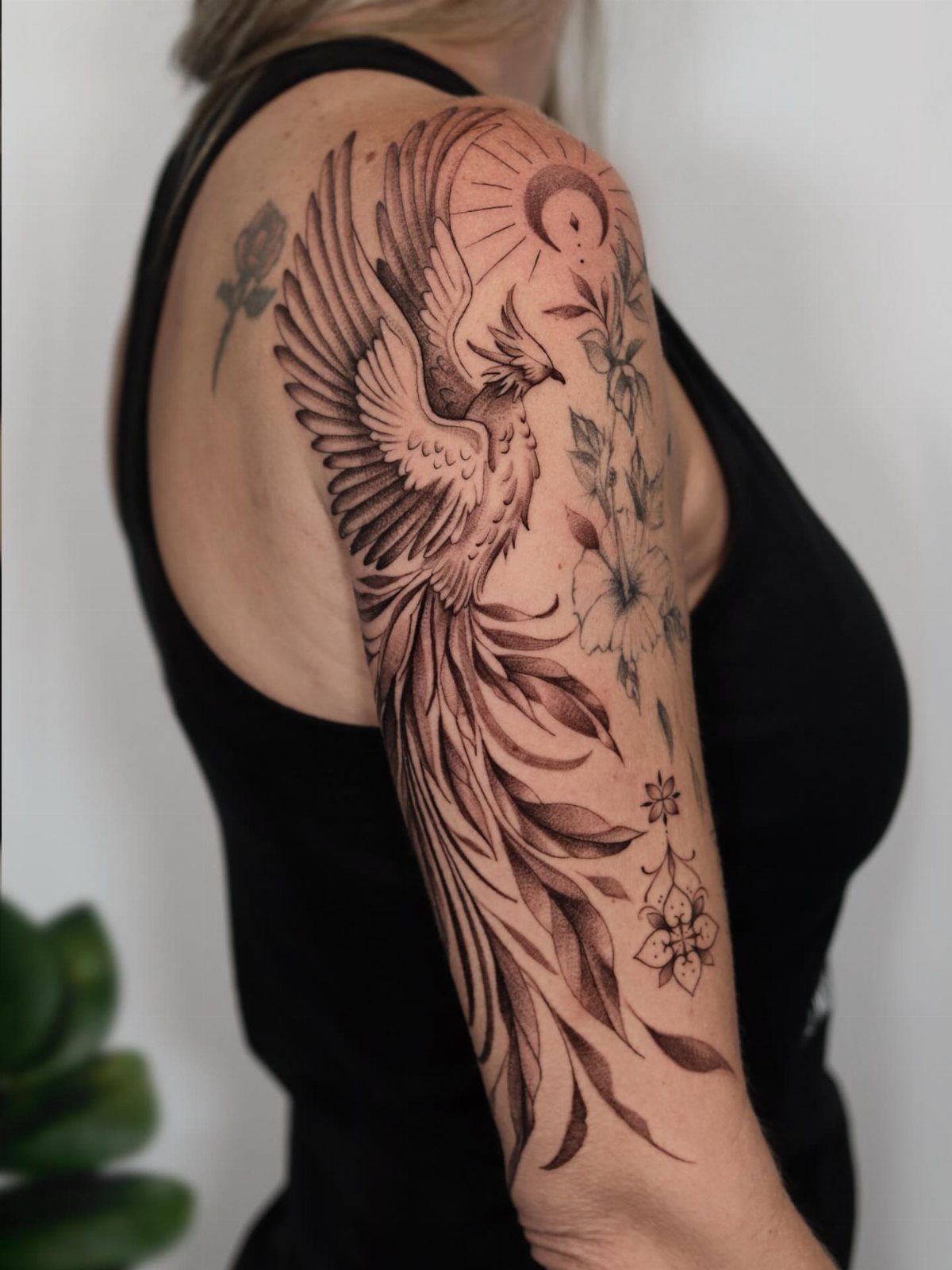 Phoenix tattoo with a crescent moon and flowers on a person's upper arm.