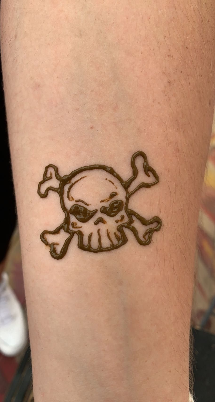 Skull and crossbones henna tattoo on a person's forearm.