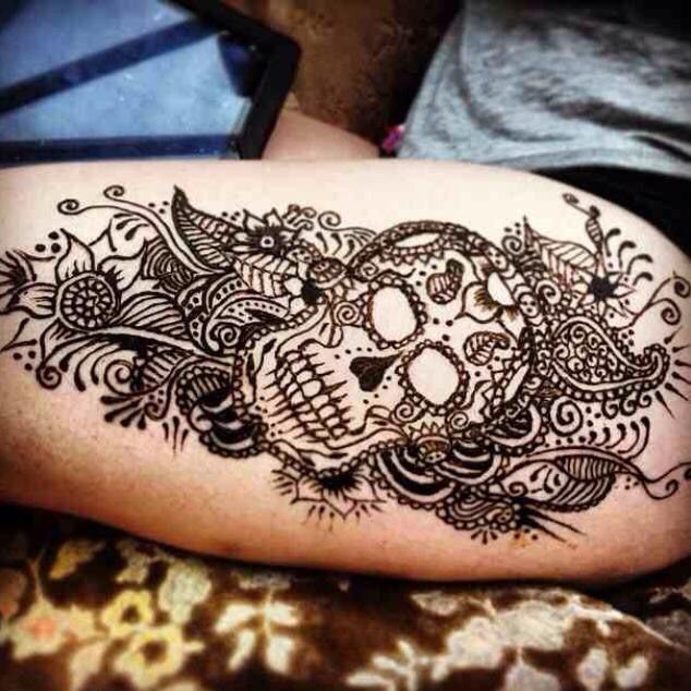Intricate black henna tattoo of a skull surrounded by floral patterns and swirls.