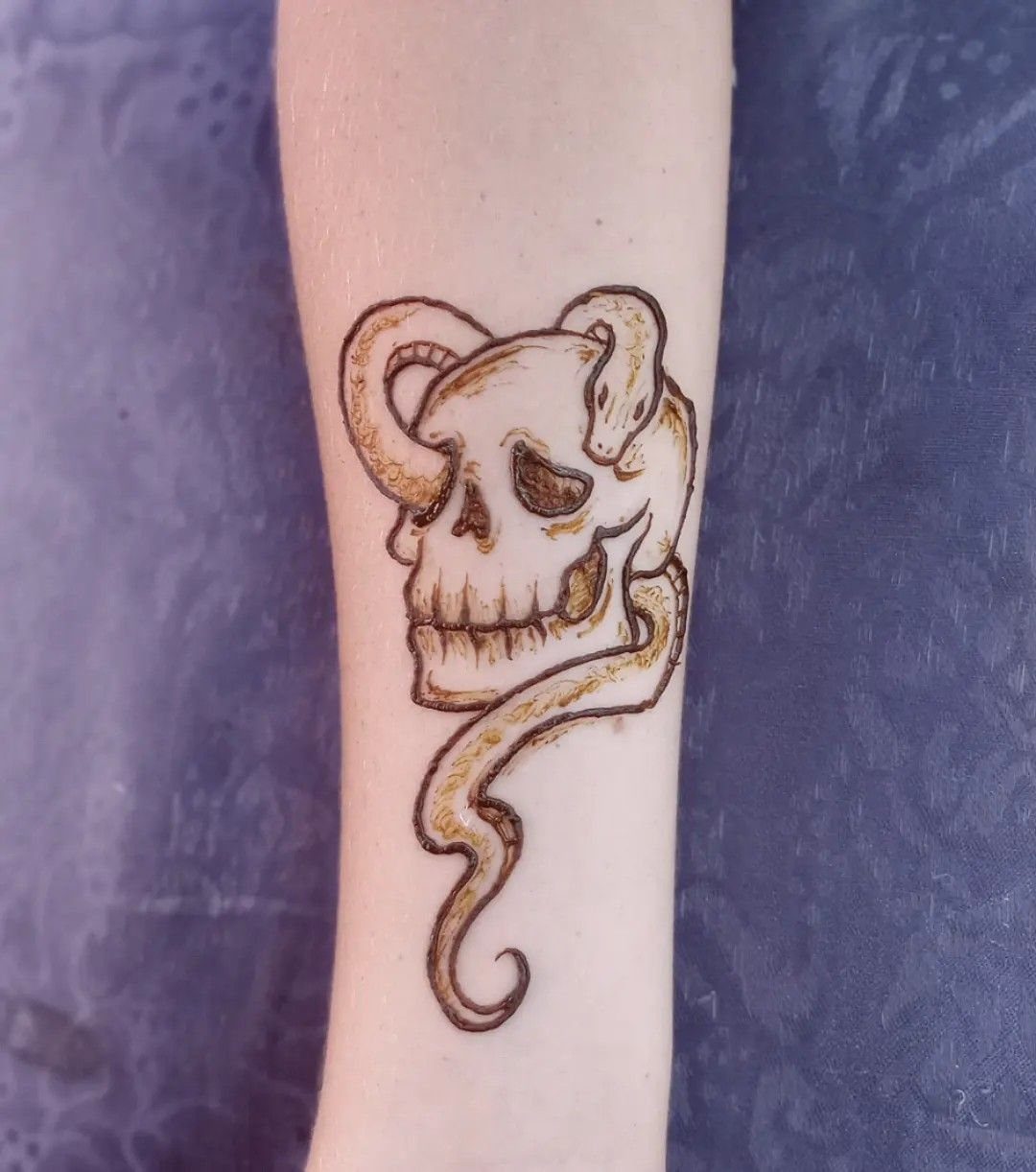 Henna tattoo of a skull with a snake coiled around it on a forearm