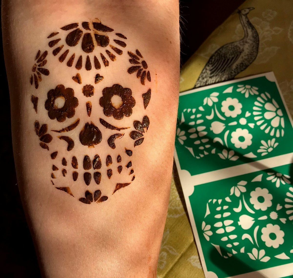 Sugar skull henna tattoo on an arm with accompanying green stencil sheets.