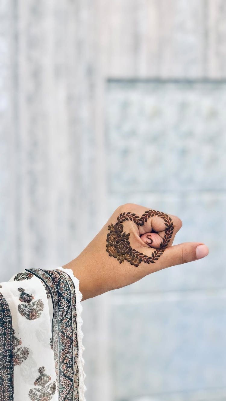 Hand with a heart-shaped henna tattoo and an embroidered white sleeve.