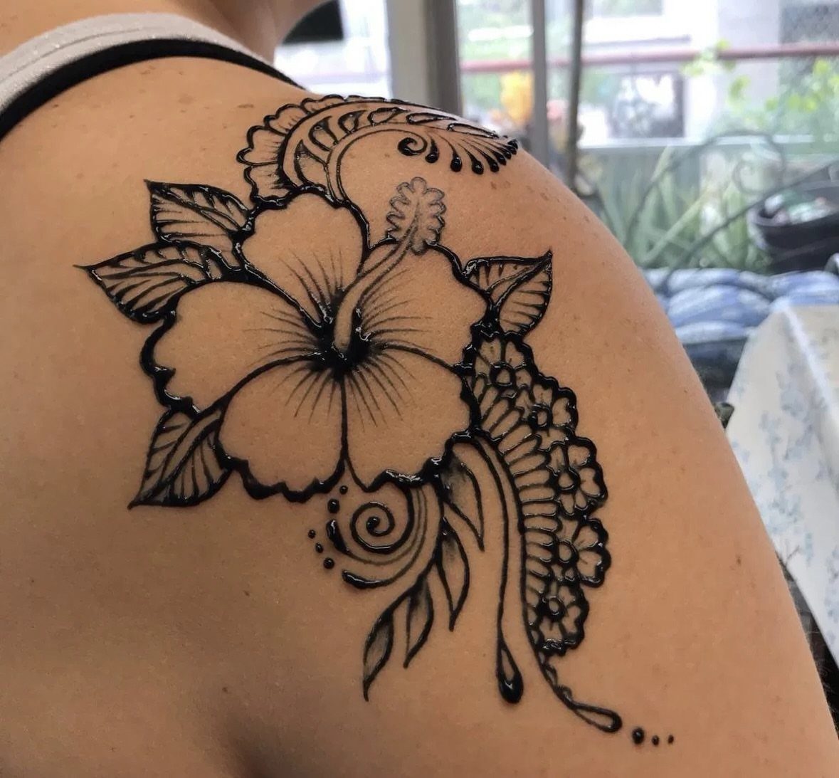 Hibiscus flower henna tattoo with swirls and leaves on a person's shoulder