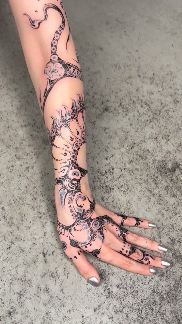 Intricate black henna tattoo sleeve covering a person's forearm, hand, and fingers.