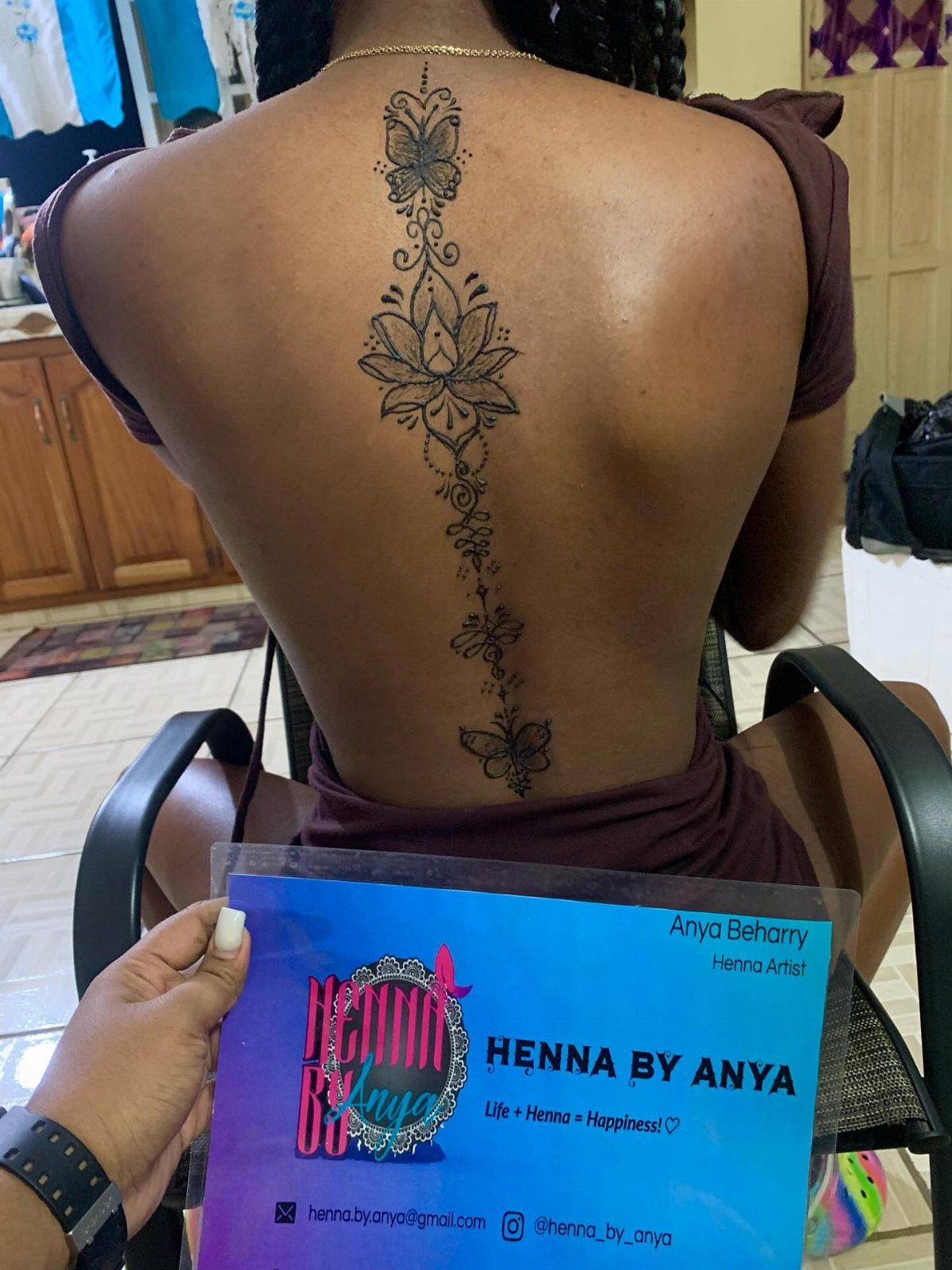 Vertical henna tattoo with lotus and butterflies on a person's back.