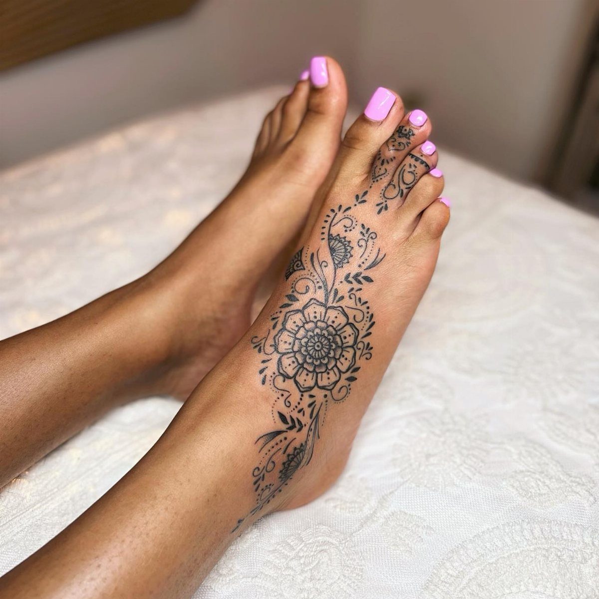 Feet with intricate black floral henna tattoo and bright pink painted toenails.