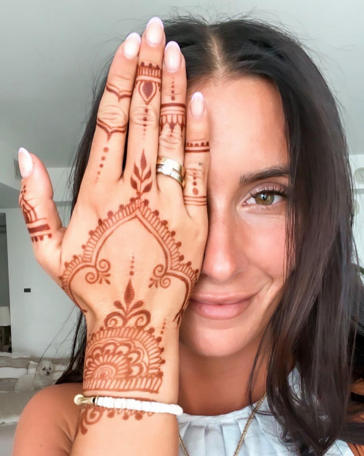 Woman's hand and wrist featuring intricate reddish-brown henna patterns and a white beaded bracelet.