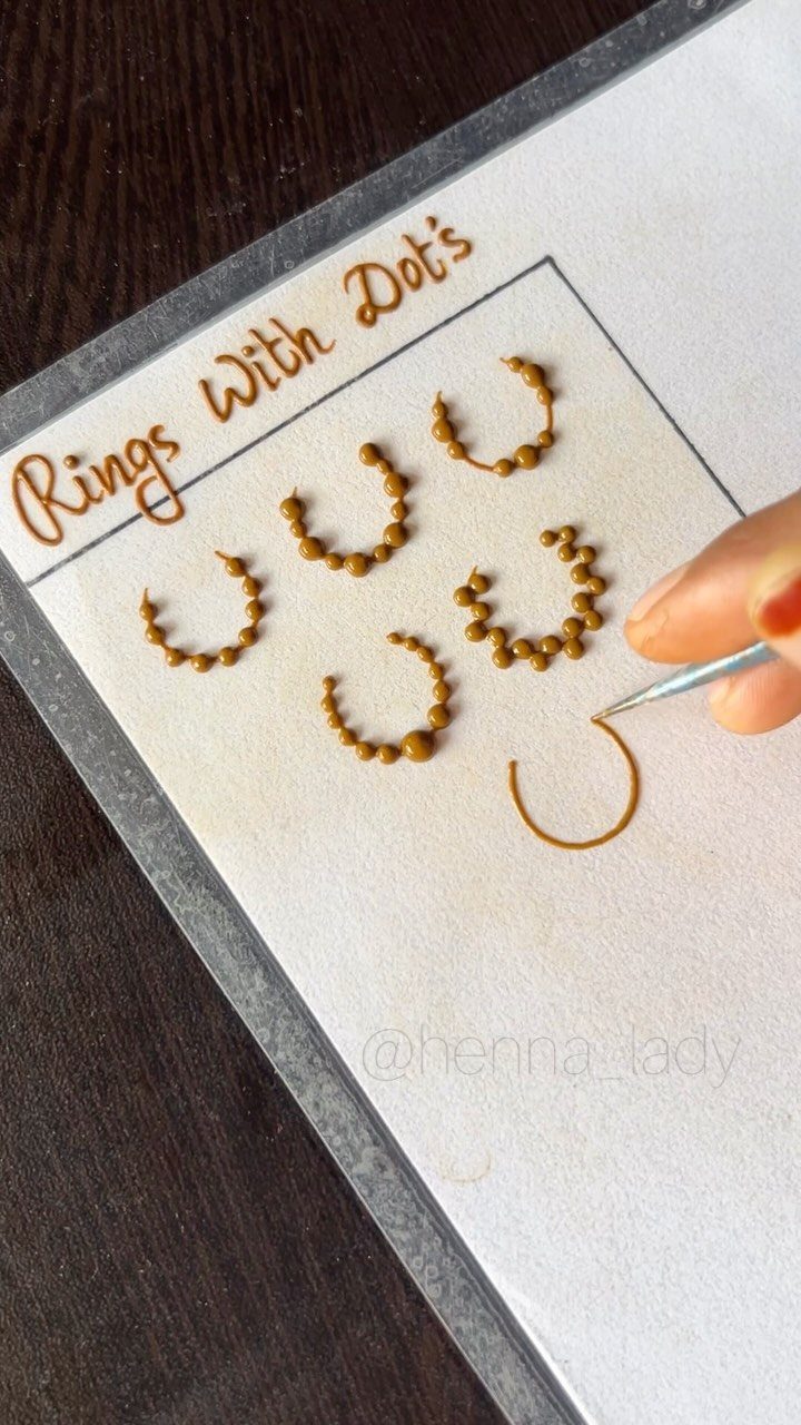 Hand drawing brown henna ring designs with dots on white paper.