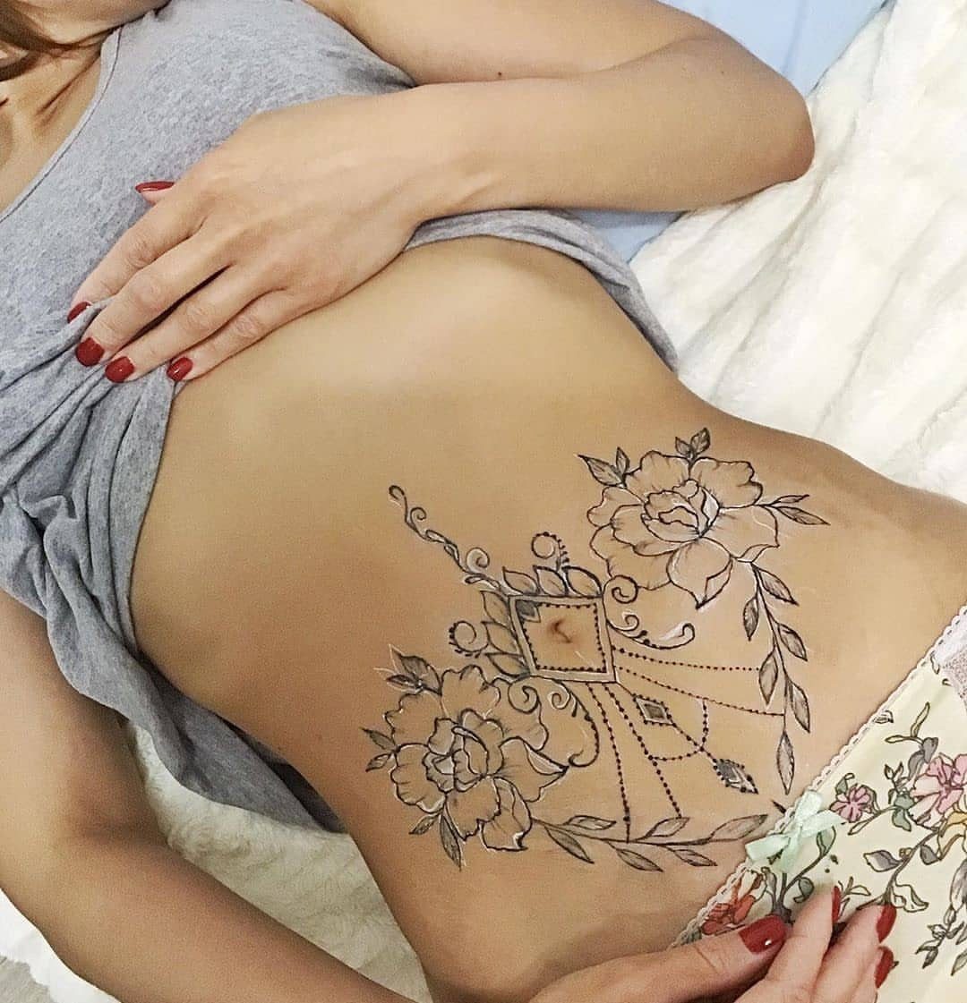 Floral henna tattoo with roses and geometric patterns on a person's stomach.