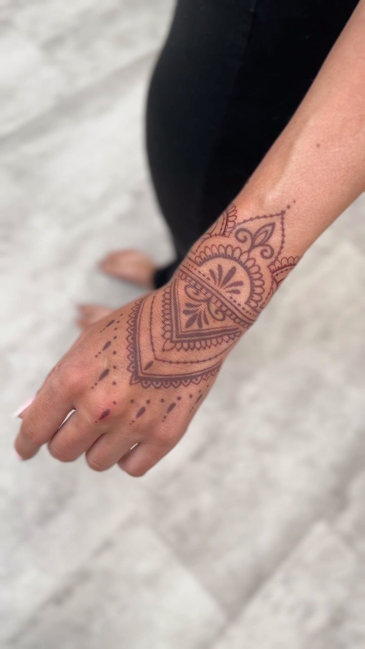 Intricate brown henna tattoo on a person's wrist and hand with floral patterns.