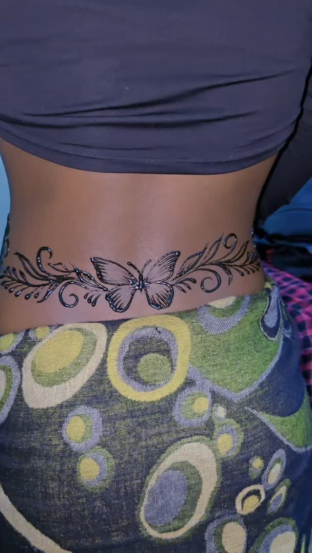 Butterfly henna tattoo on a person's lower back with floral swirls and patterned clothing.