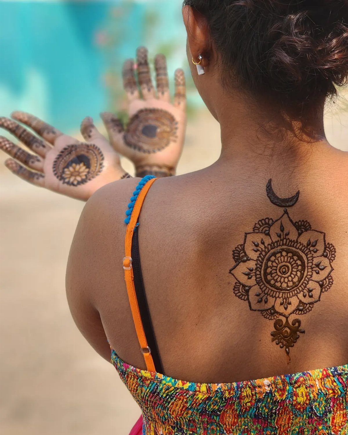 Henna mandala tattoo on a woman's back with a crescent moon detail.