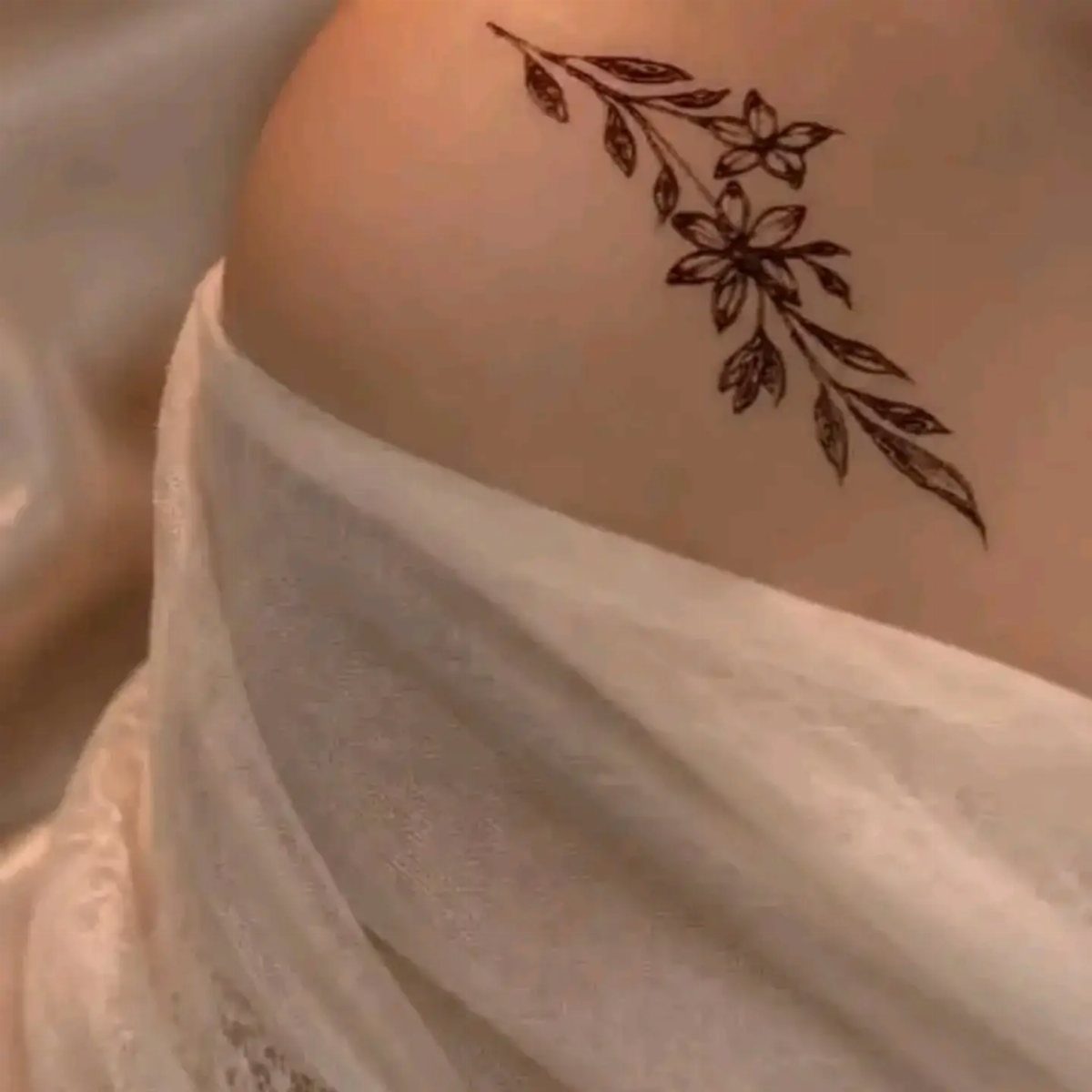Floral henna tattoo of a branch with leaves on a person's shoulder.