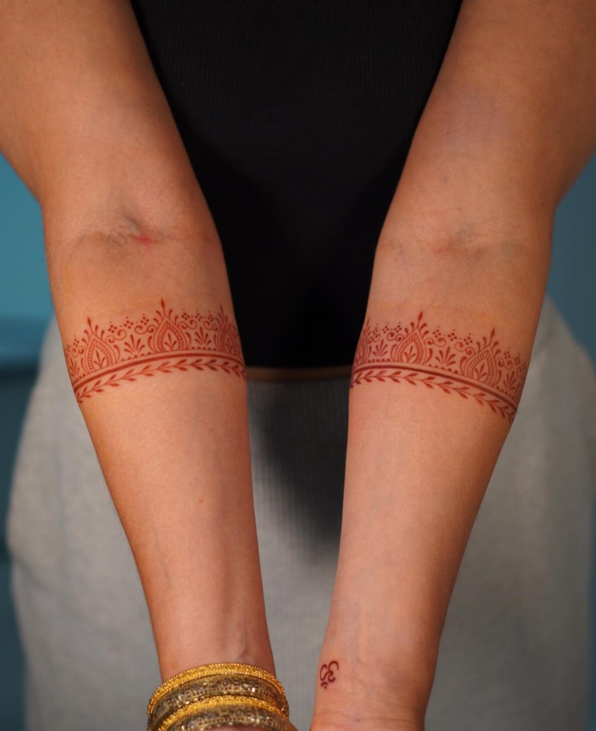 Henna tattoos with floral patterns wrapping around both forearms of a person.