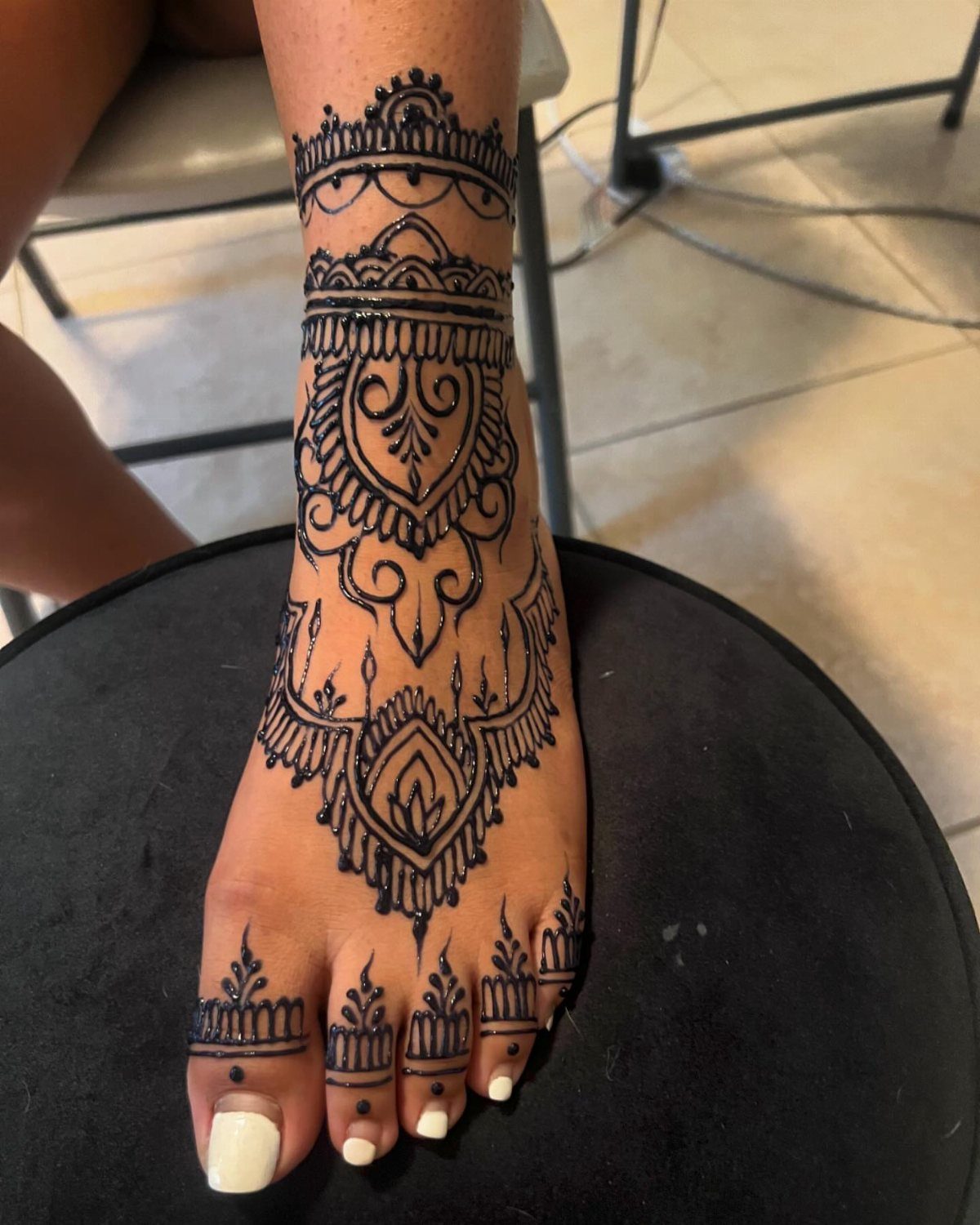 Foot with intricate black henna tattoo designs covering the ankle and top of foot.
