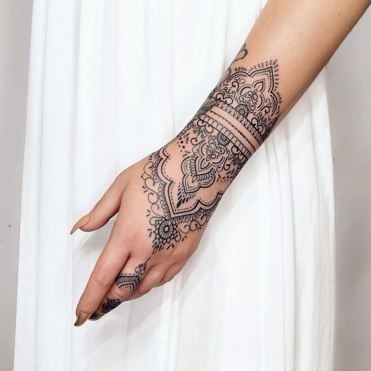 Intricate black henna tattoo designs on a person's hand and wrist against white clothing