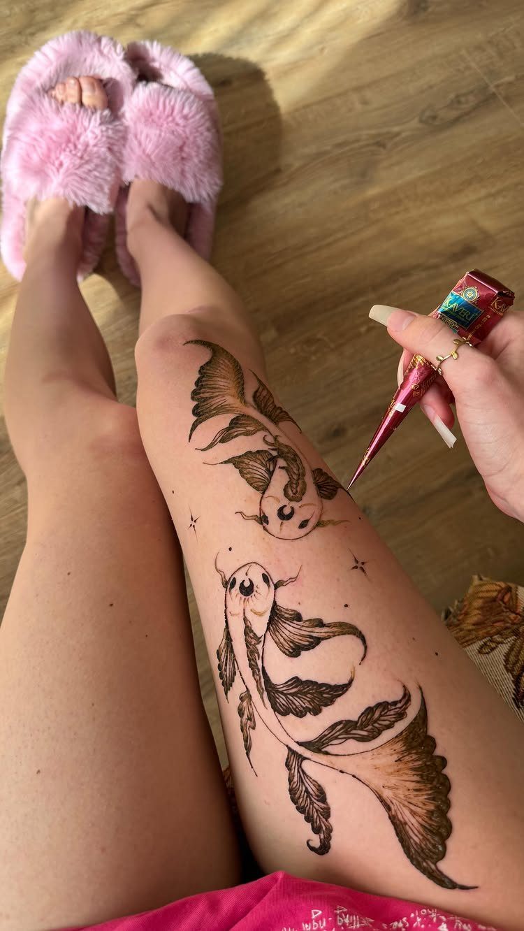 Henna fish designs on a leg being applied with a henna cone