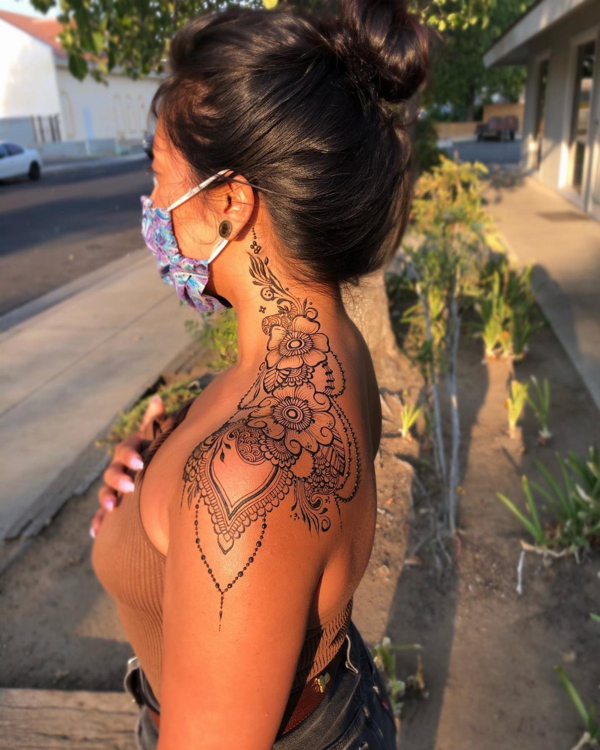 Woman with an intricate brown henna tattoo on her neck and shoulder outdoors