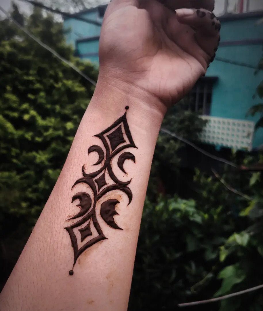 Geometric henna tattoo with bold diamond shapes on a person's forearm.