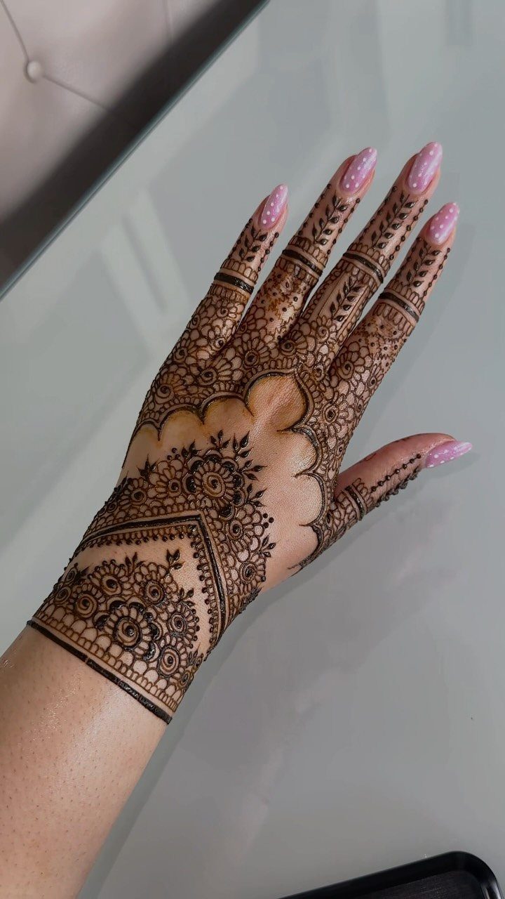 Hand with intricate brown henna floral designs and long pink manicured nails.