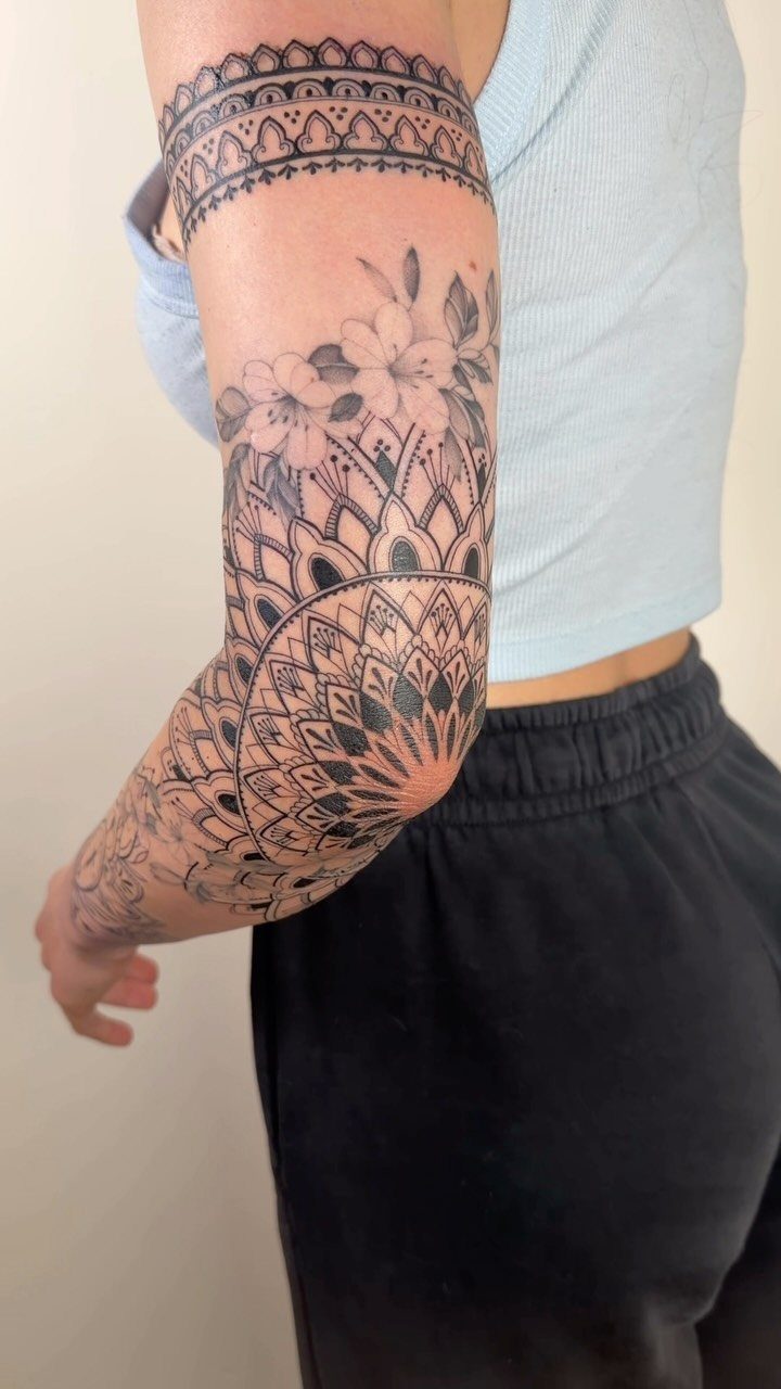 Henna sleeve tattoo on an arm featuring a mandala and floral patterns.
