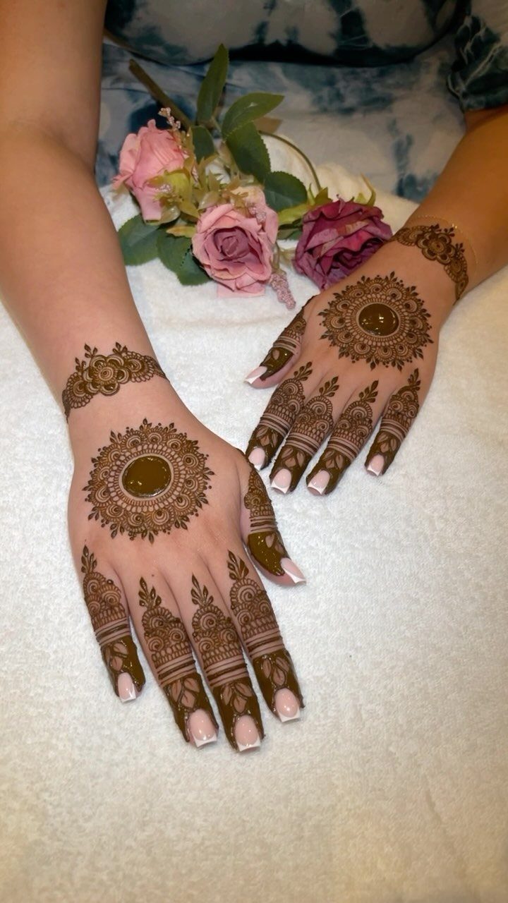 Henna mandala designs on the backs of two hands with pink roses nearby
