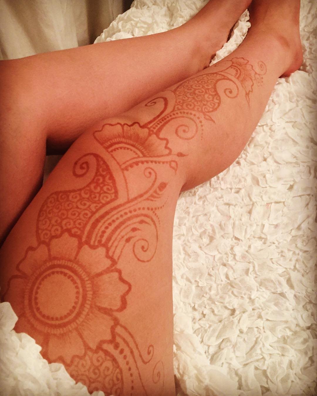Henna tattoo on a leg featuring paisley motifs and floral designs on white fabric.