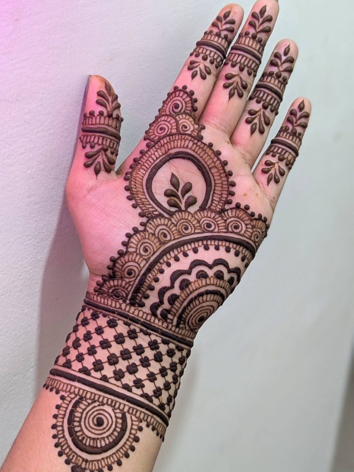 Intricate brown henna tattoo design covering a person's palm and wrist