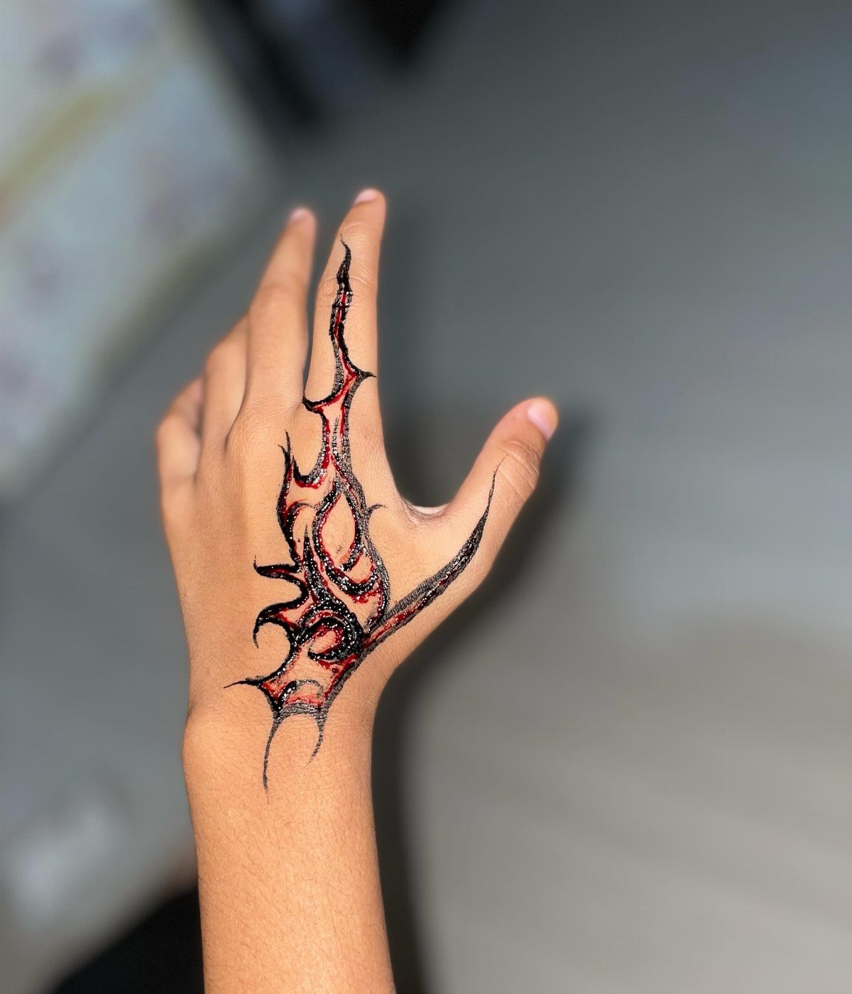 Hand with a black and red tribal henna tattoo design extending to the finger.