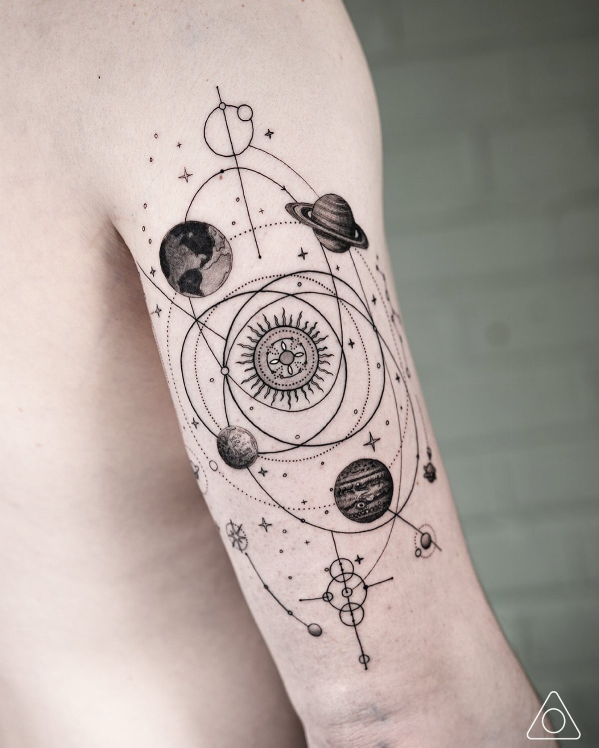 Celestial tattoo on an arm featuring planets, a sun, and orbiting geometric lines.