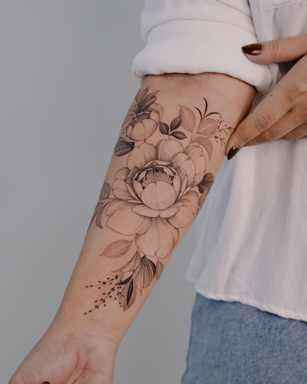 Fine line floral tattoo of a peony on a person's forearm
