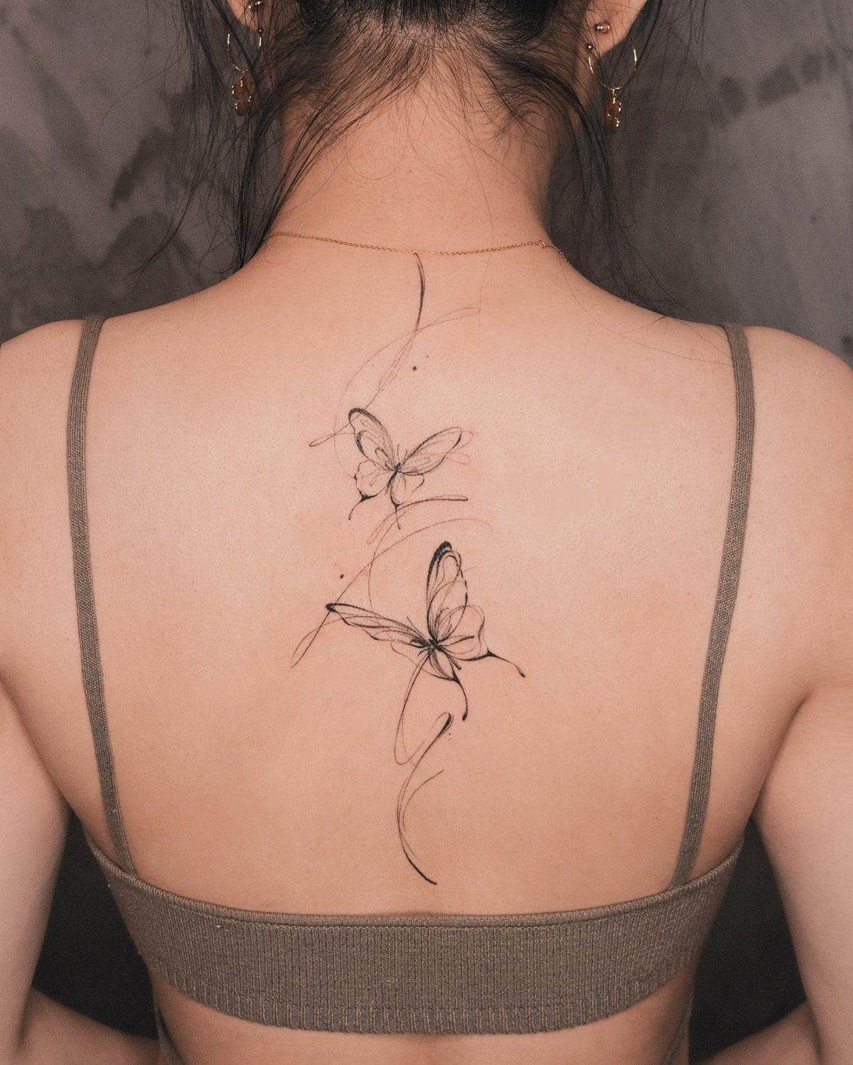 Two minimalist butterfly line art tattoos on a person's upper back and spine.