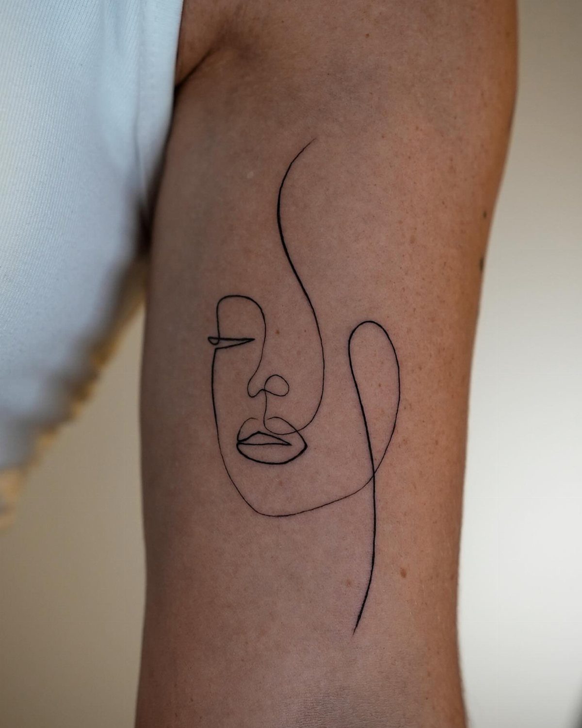 Single line portrait tattoo of a face on a person's arm