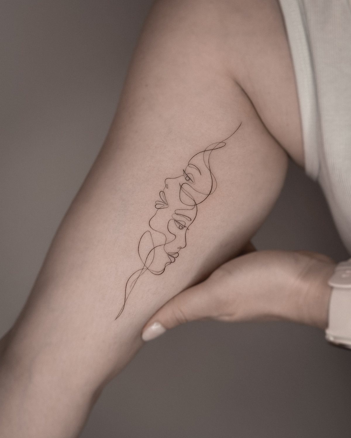 Single line tattoo of two overlapping faces in profile on a person's arm
