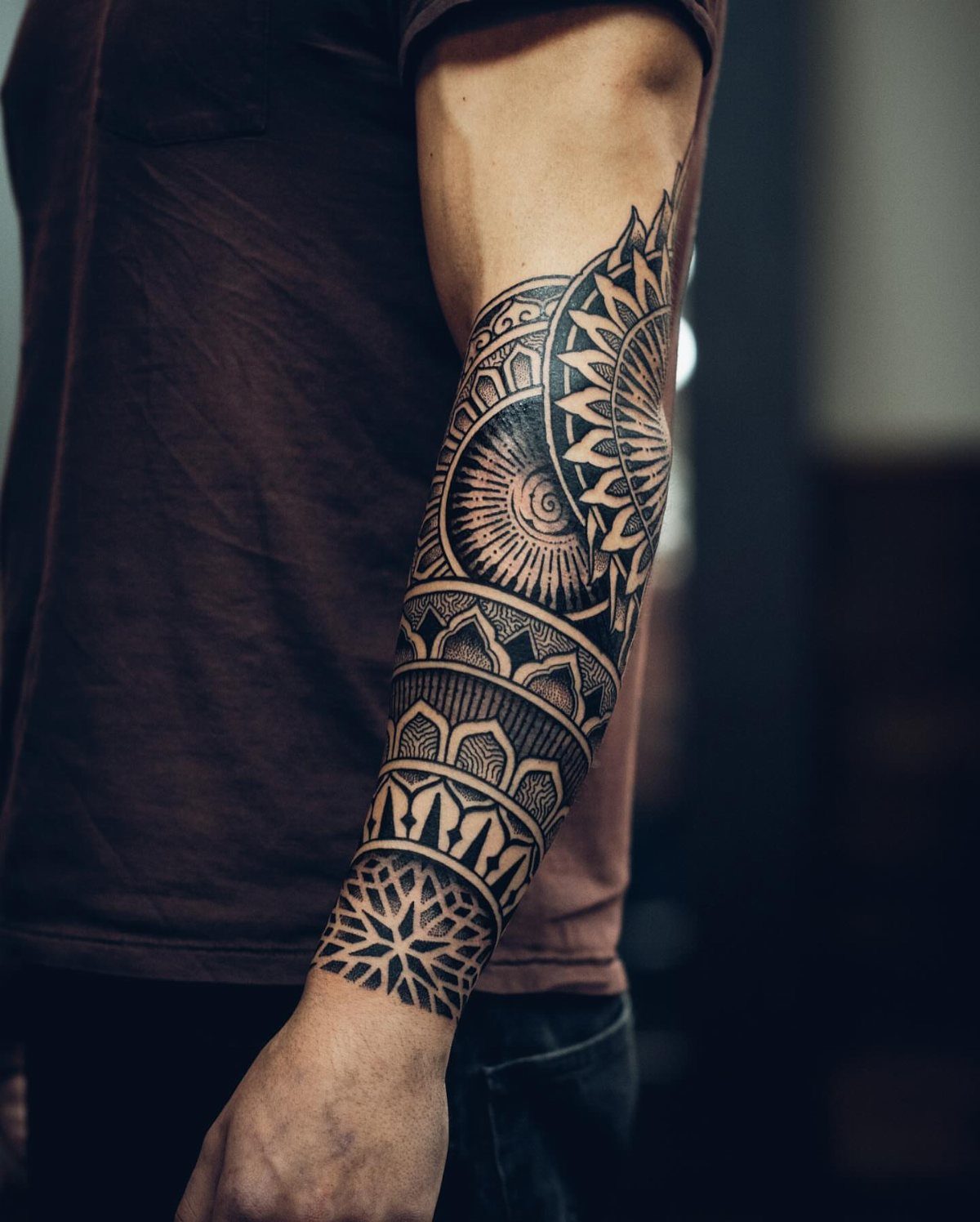 Bold black ink mandala tattoo with geometric patterns on a person's forearm.