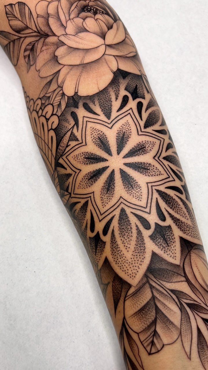 Floral mandala tattoo on an arm with a peony and geometric patterns.