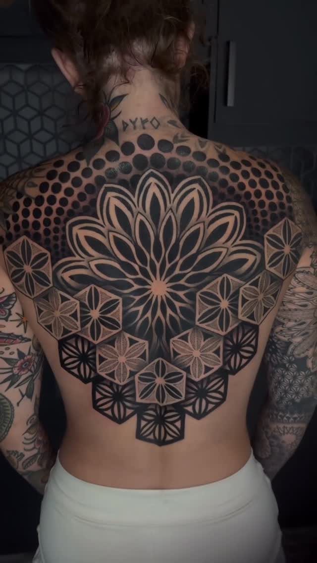 Large black ink mandala tattoo with geometric patterns covering a person's upper back.