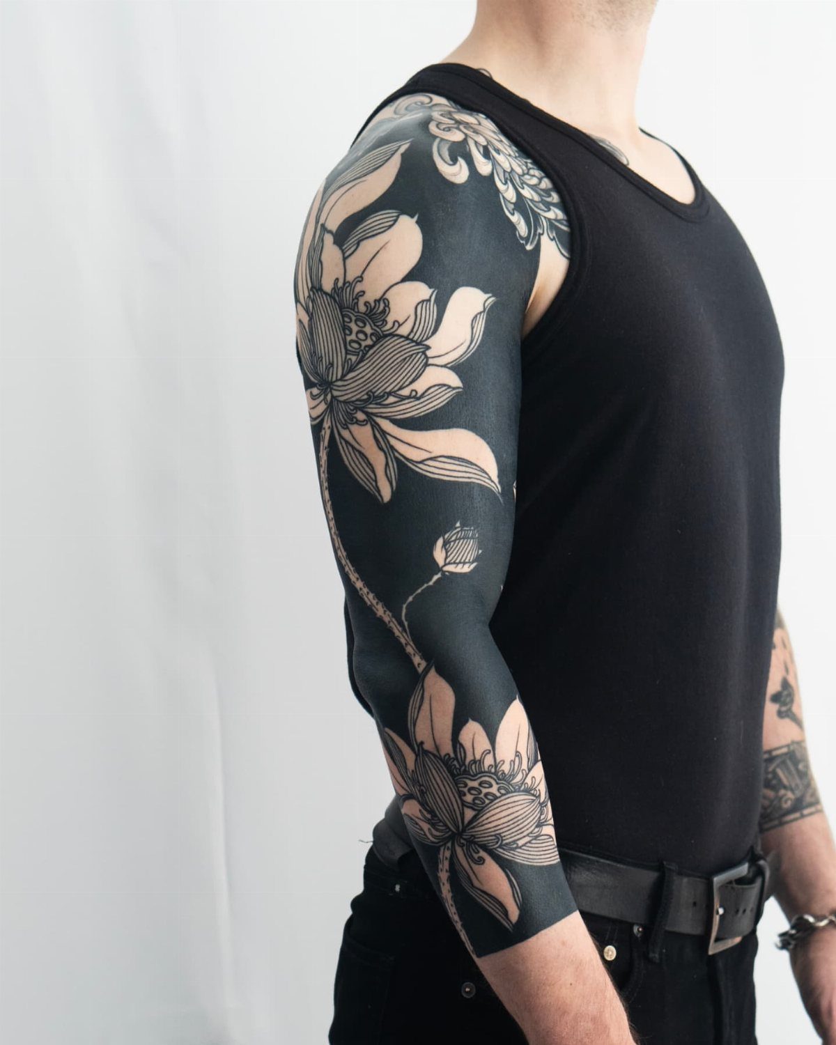 Blackout sleeve tattoo on an arm featuring light-colored lotus flower designs.