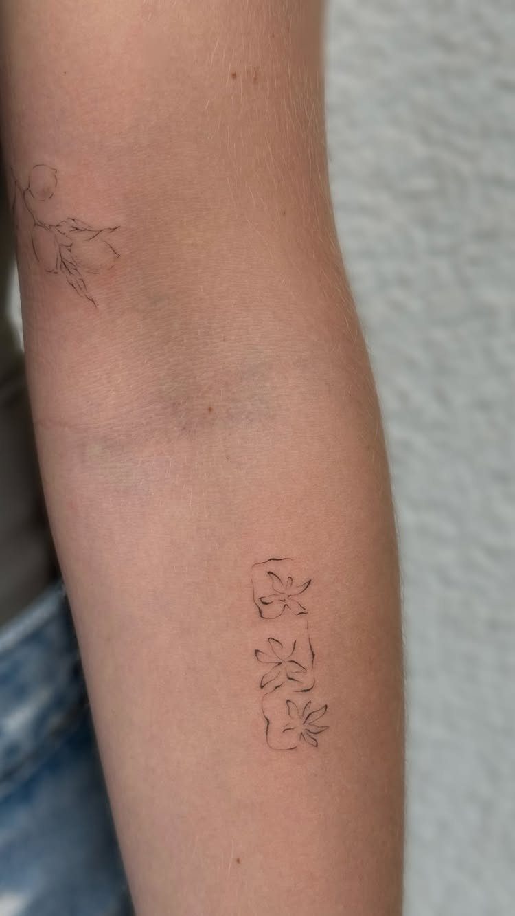 Forearm with two small, delicate black ink fine line botanical flower tattoos.