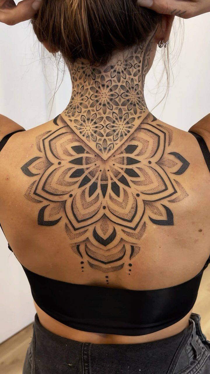 Geometric mandala tattoo on a person's upper back and neck in black ink.